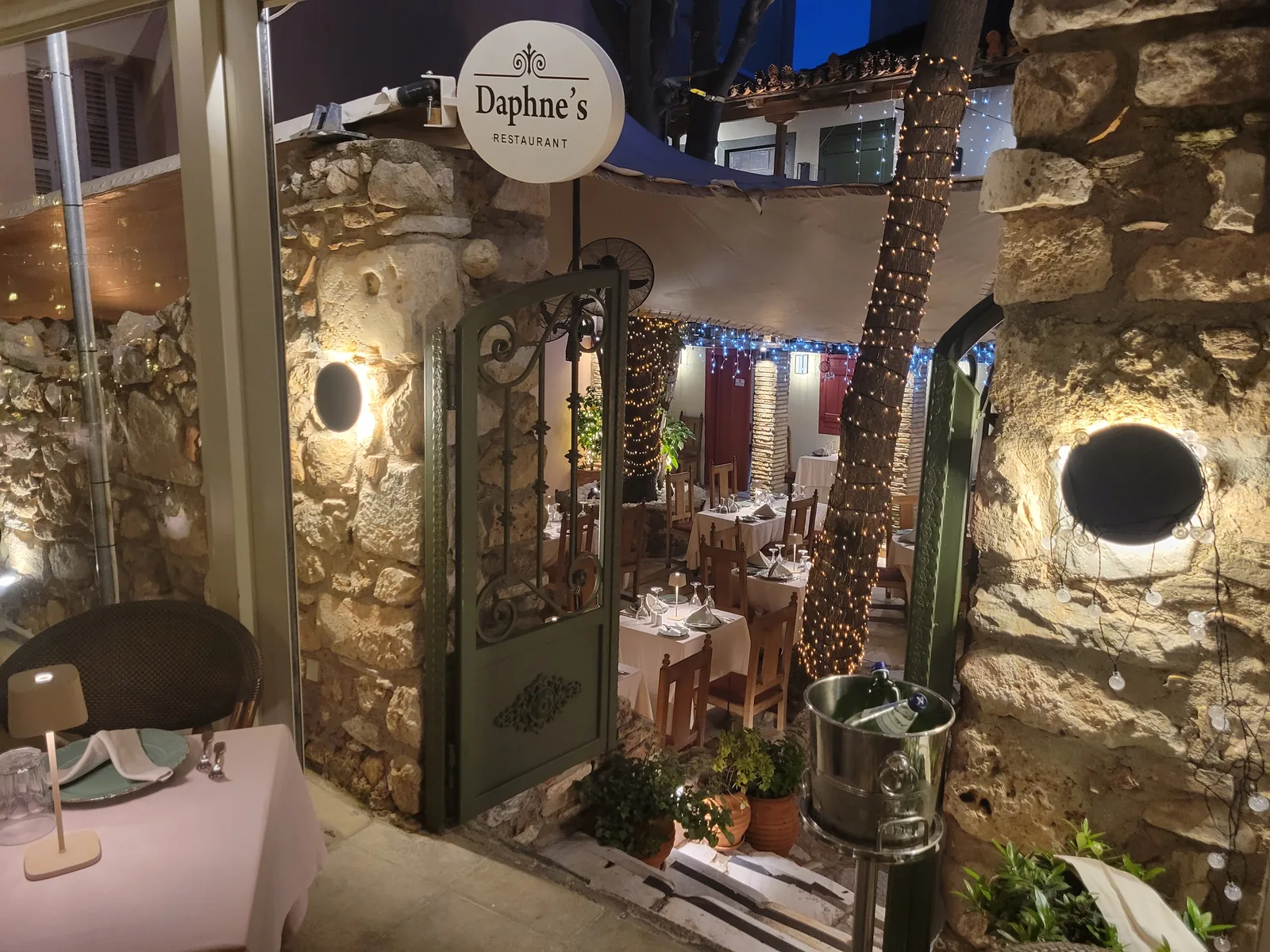 Daphne's garden restaurant — wall-grazing light on old stone, fairy-lit palms and candlelit tables, Athens