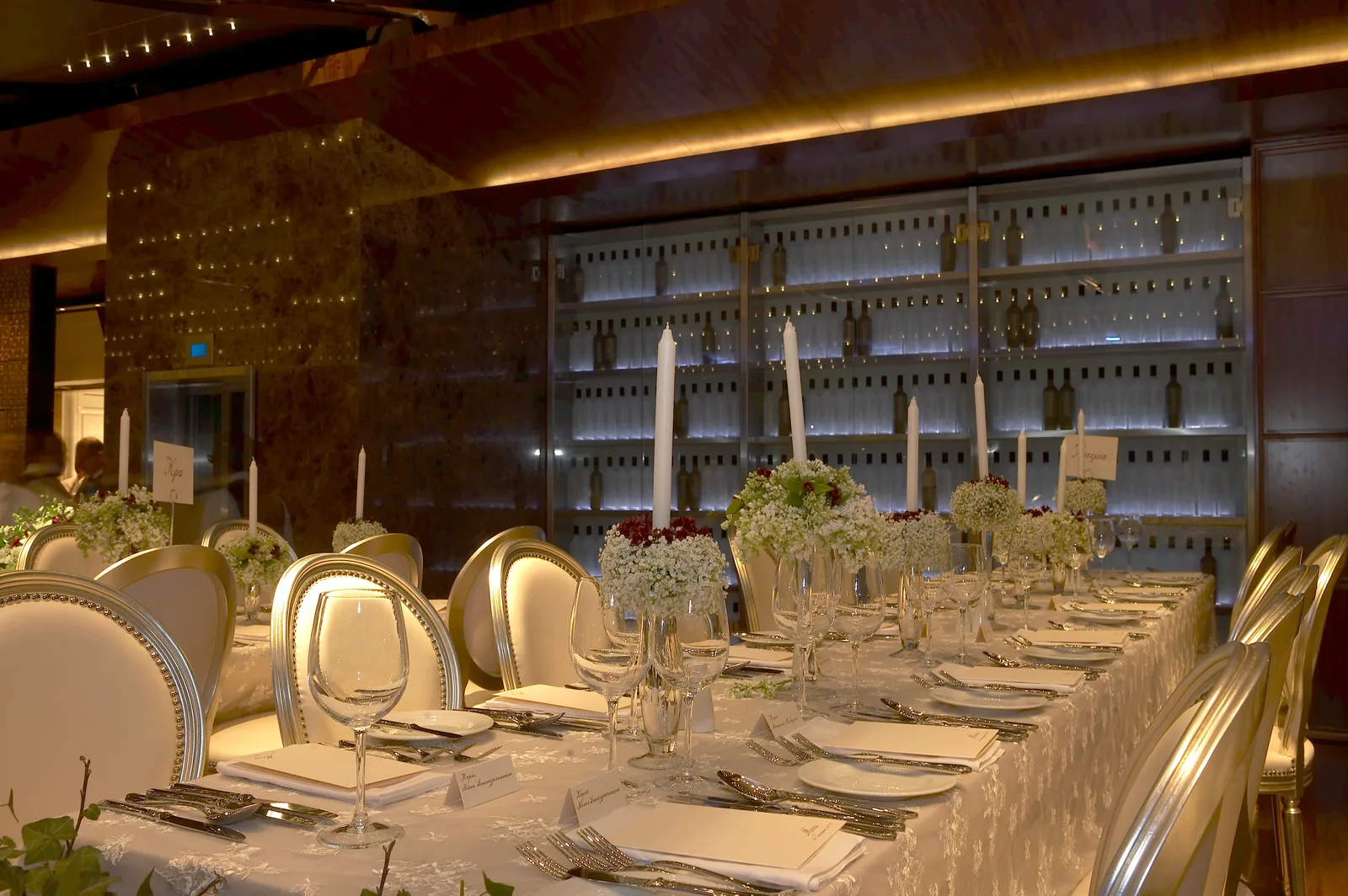 Dionysos Zonars restaurant — warm dining lighting and a backlit wine wall with Acropolis view, Athens