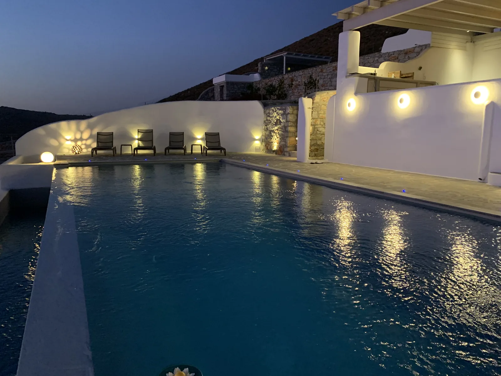 Cycladic villa in Naxos — recessed wall sconces and submerged pool lighting on a terrace at dusk