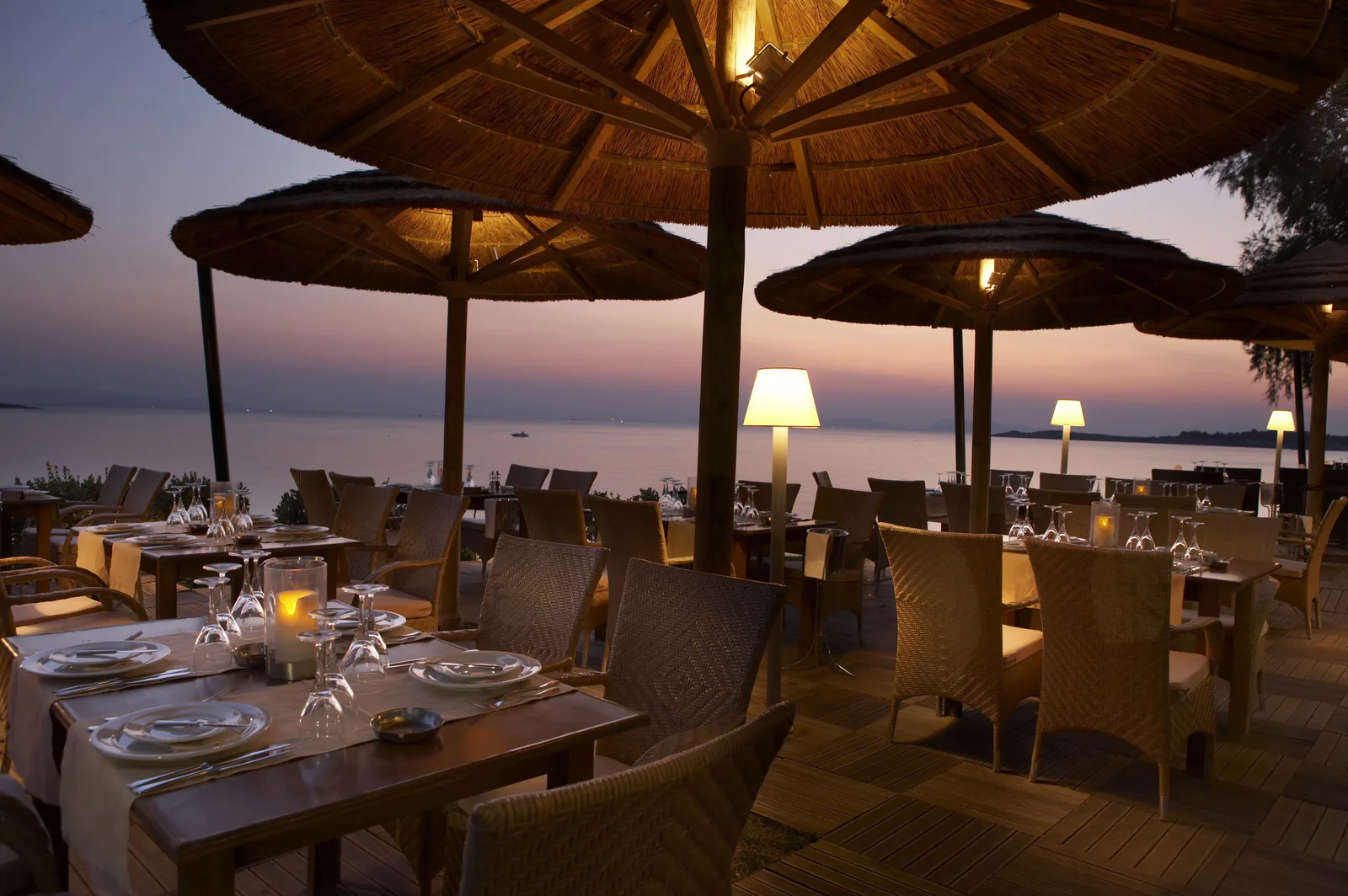 Notos seaside restaurant at sunset — cordless table lamps and warm low light over a sea-view terrace, Voula